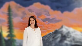 Mrs. Bell standing in front of a mural of sunset over mountains.Picture